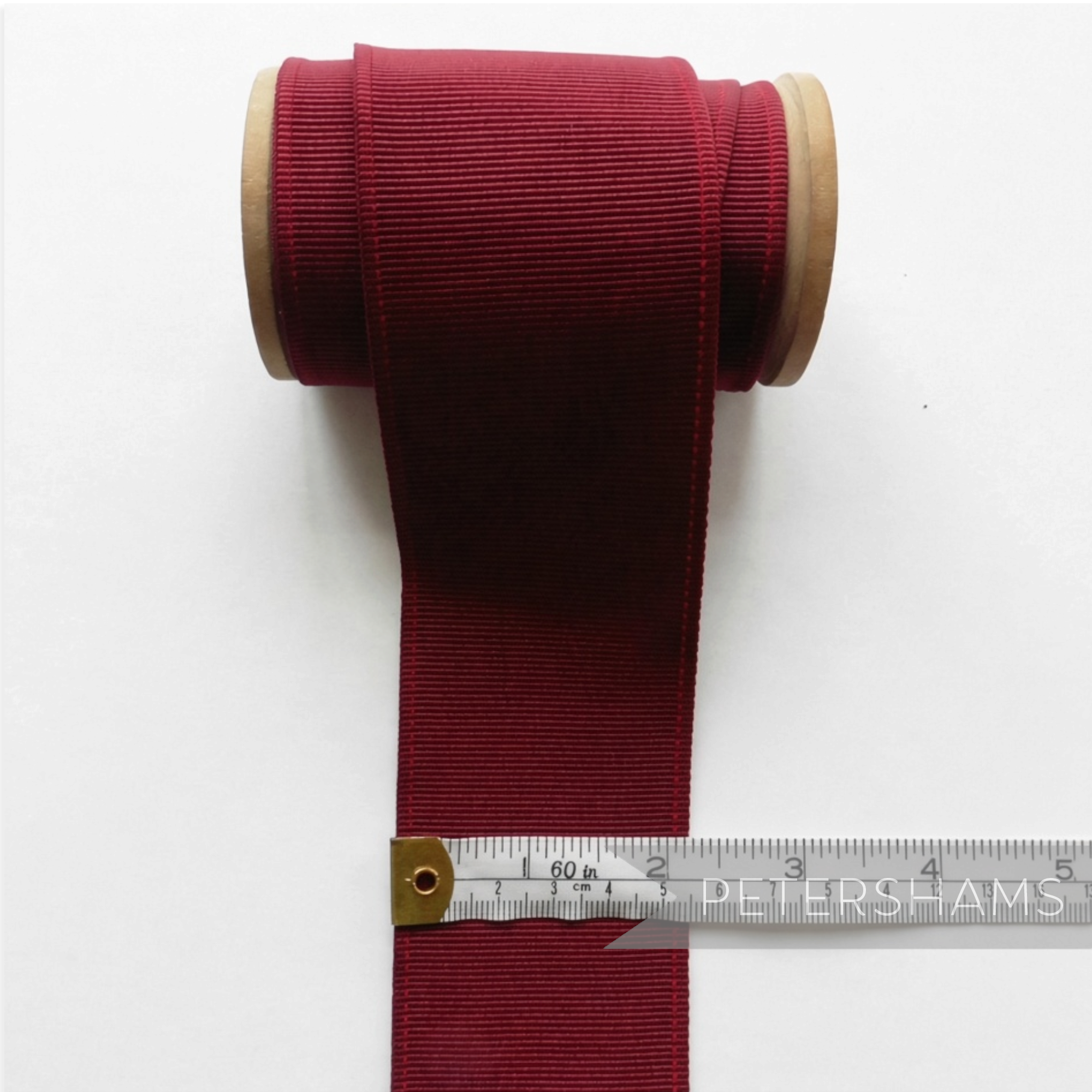 Petershams Millinery Supplies 53mm wide deep red ribbed belting ribbon on a wooden spool with a measuring tape.