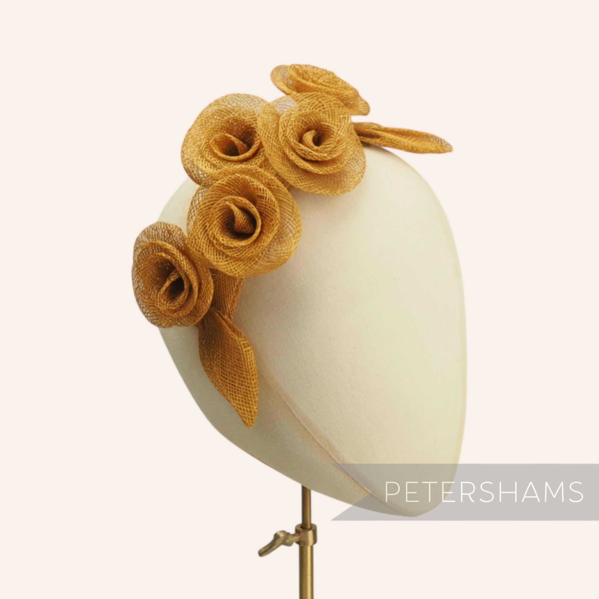 Petershams Millinery Supplies gold sinamay flower and leaf hat mount. Features five rolled flowers and two leaves.
