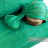 Petershams Millinery Supplies green polyester abaca fabric with a slightly glossy, rustic texture and wavy threading. Ideal for bows and loops.