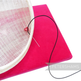Petershams Millinery Supplies black 1.5mm knotted hat elastic being sewn onto a white fascinator base