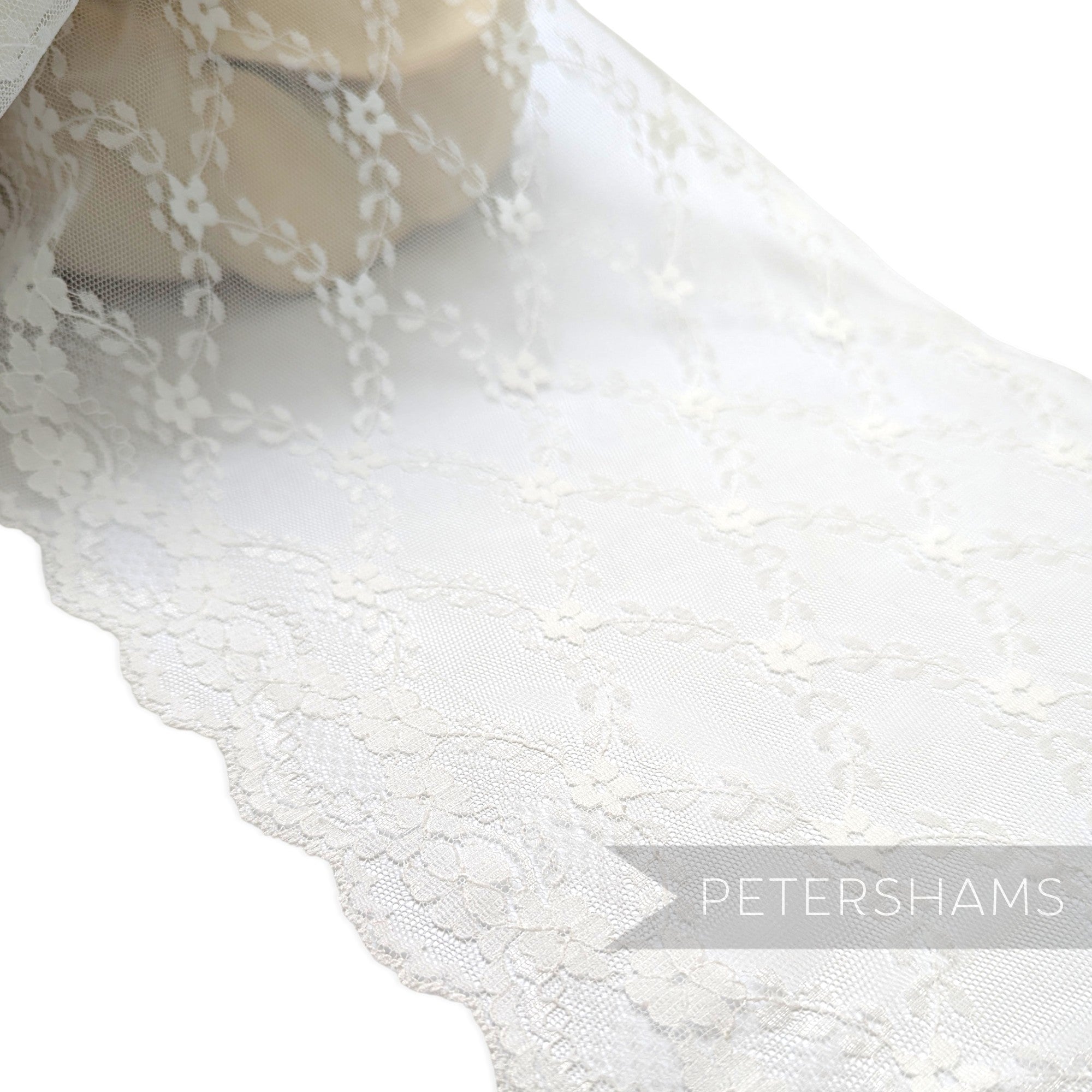Petershams Millinery Supplies 25cm wide white sheer lace trim featuring a floral scale pattern and scalloped edges.