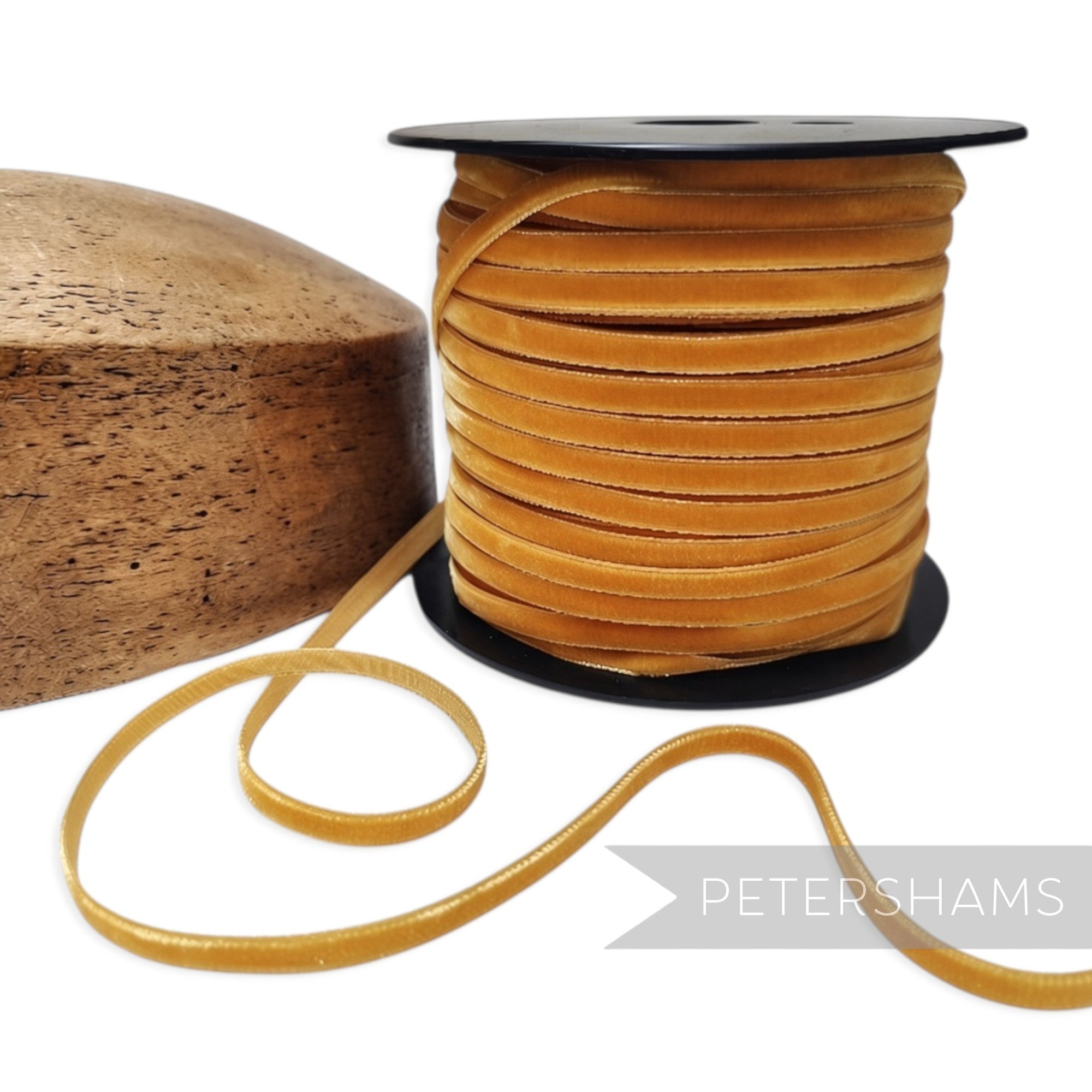 Petershams Millinery Supplies 7mm gold French velvet ribbon on a spool next to a wooden hat block