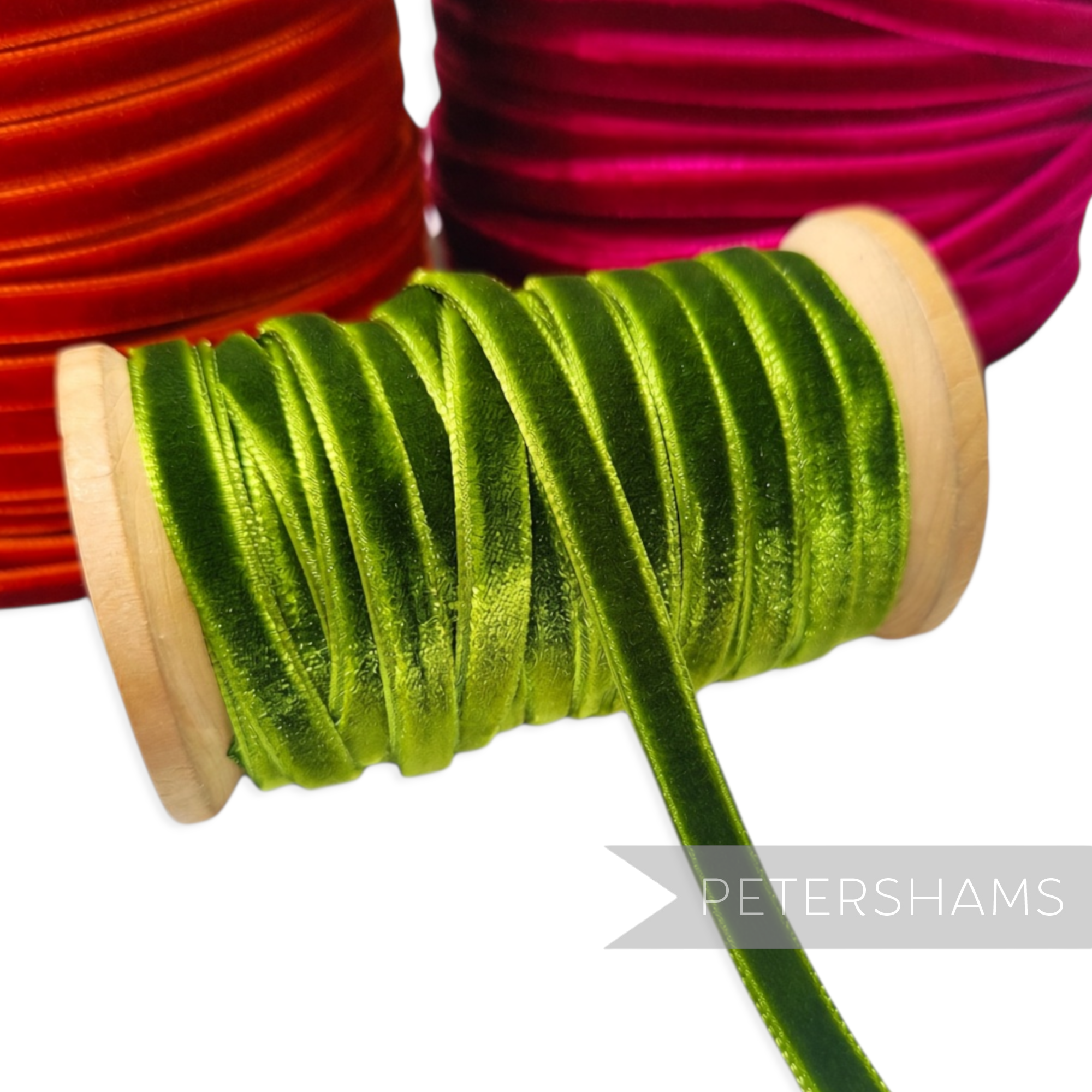 Petershams Millinery Supplies 7mm green French velvet ribbon on a wooden spool with red and pink rolls in background