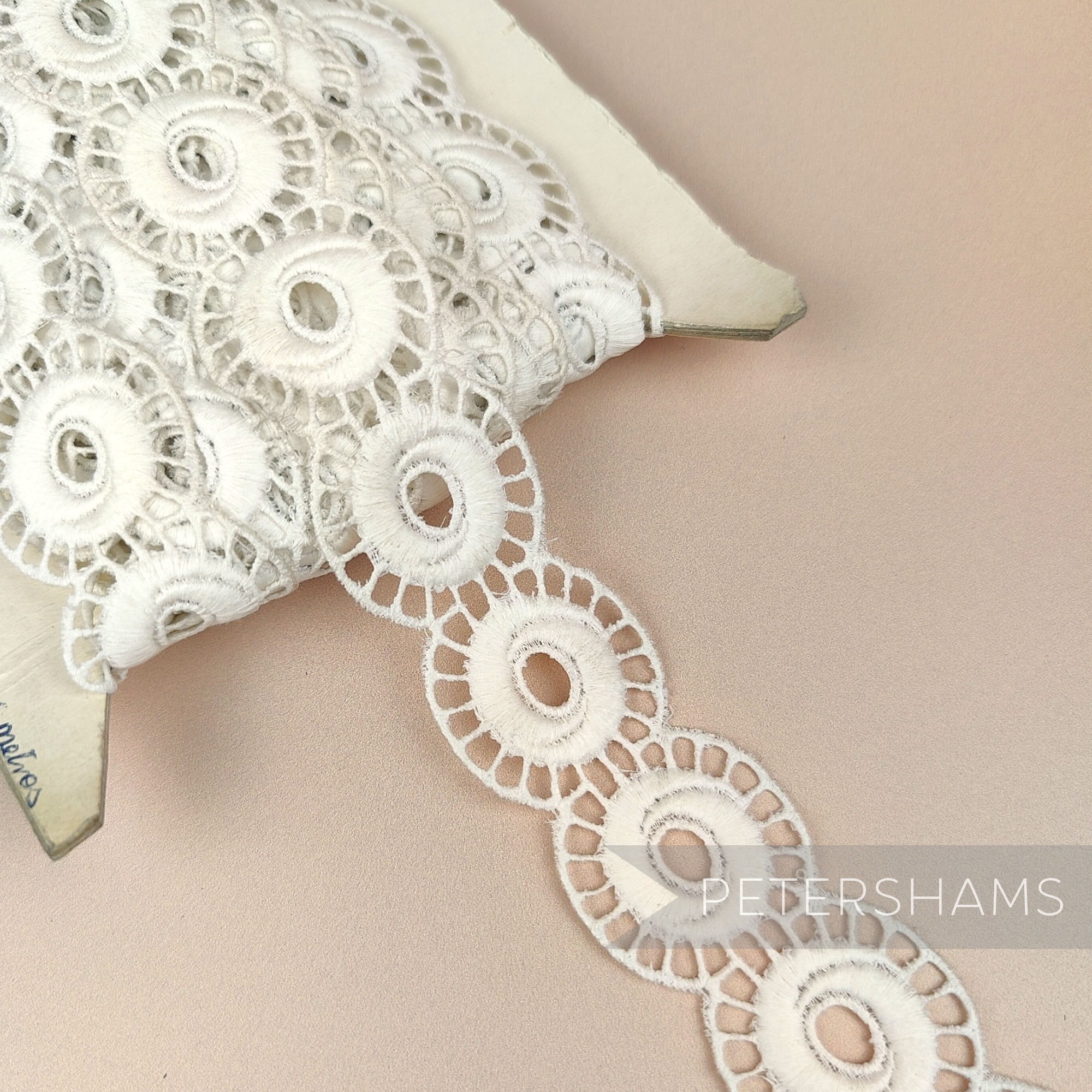 Petershams Millinery Supplies vintage 1950s ivory cotton guipure lace trim with an open whirl design on a spool.