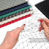 Petershams Millinery Supplies black wide diamond merry widow veiling held by hands with stacked fabric rolls behind