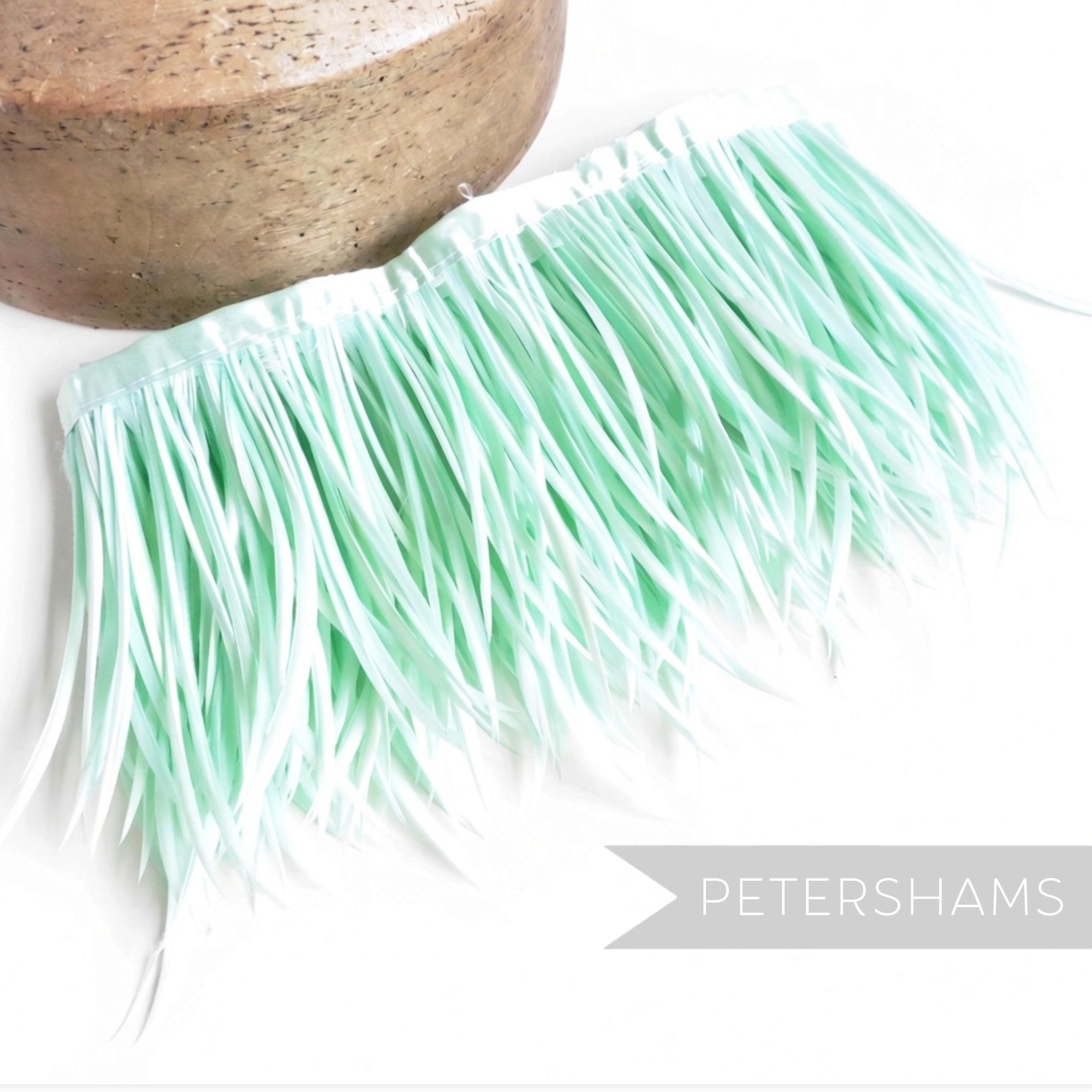Petershams Millinery Supplies mint green goose biot feather fringe on a satin ribbon binding next to a wooden block.