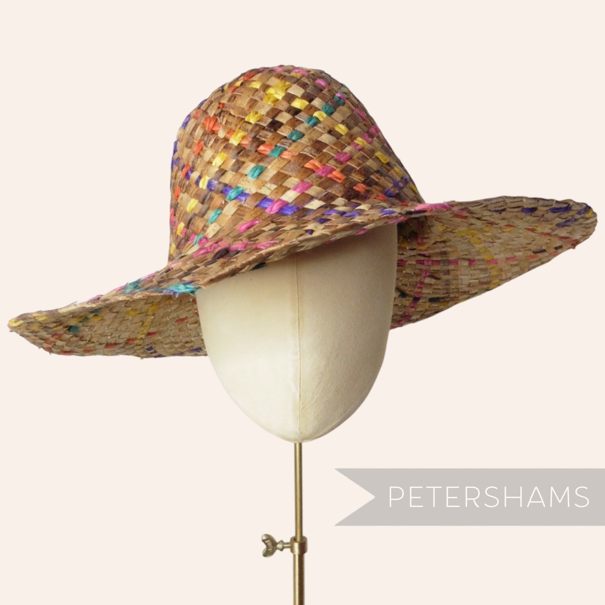Petershams Millinery Supplies dark straw capeline hat body with woven rainbow coloured accents on a millinery head.
