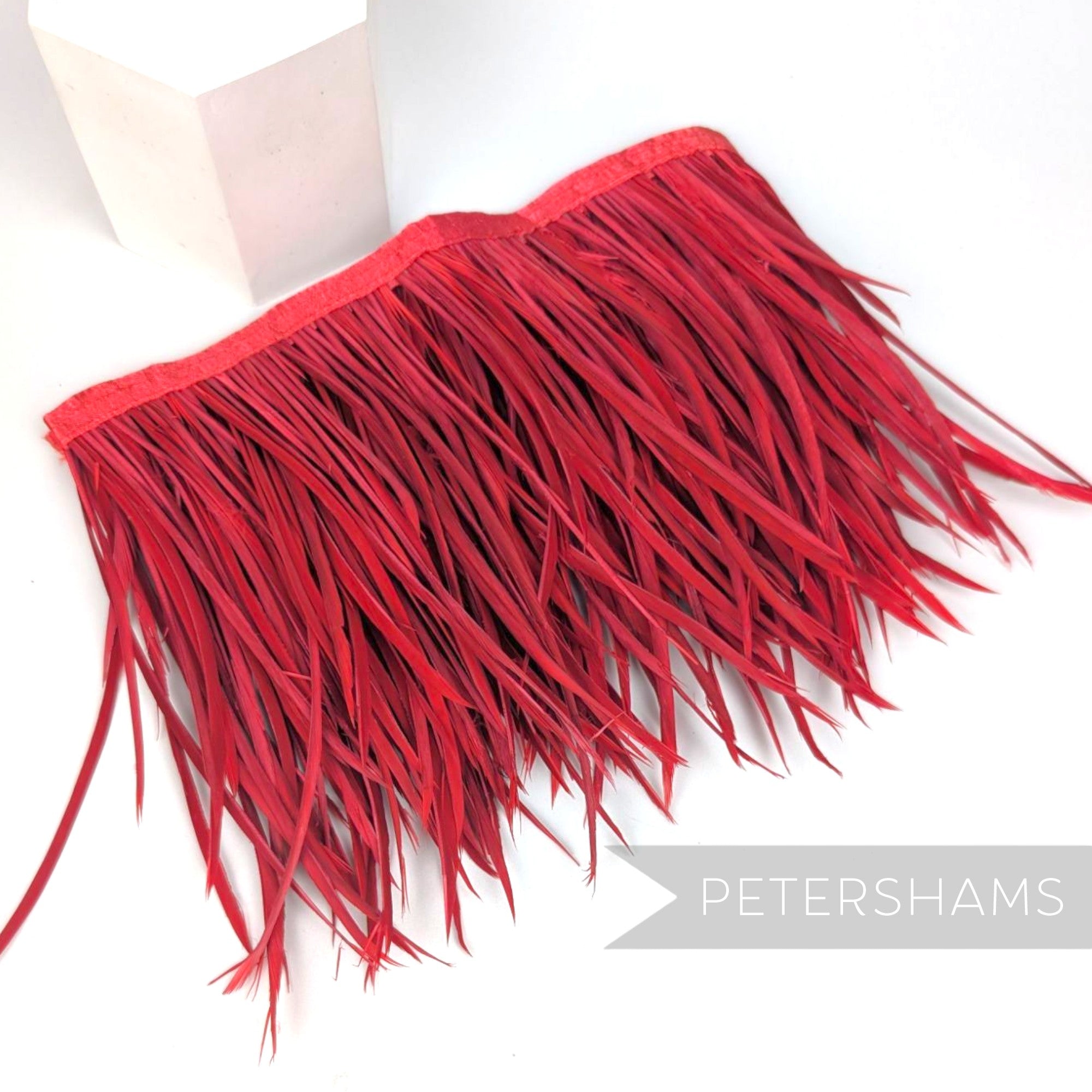 Petershams Millinery Supplies extra long red goose biot feather fringe on a stitched satin ribbon binding.