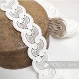 Petershams Millinery Supplies vintage white cotton guipure lace trim with a scalloped swirl design on a wooden block