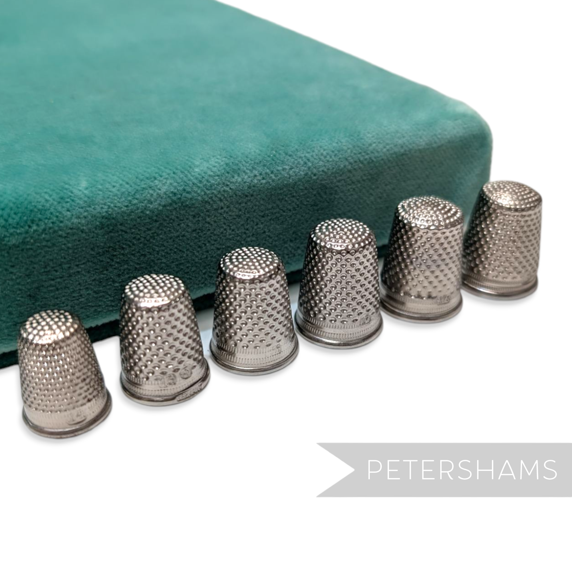 Petershams Millinery Supplies vintage German steel thimbles in various sizes arranged in a row on a green velvet base.