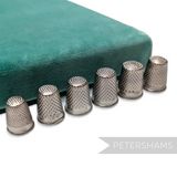 Petershams Millinery Supplies vintage German steel thimbles in various sizes arranged in a row on a green velvet base.