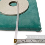Petershams Millinery Supplies 10mm white buckram tape roll on a teal velvet surface with a measuring tape
