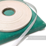 Petershams Millinery Supplies 10mm white buckram tape roll for hat making and structural trim on a green velvet base.