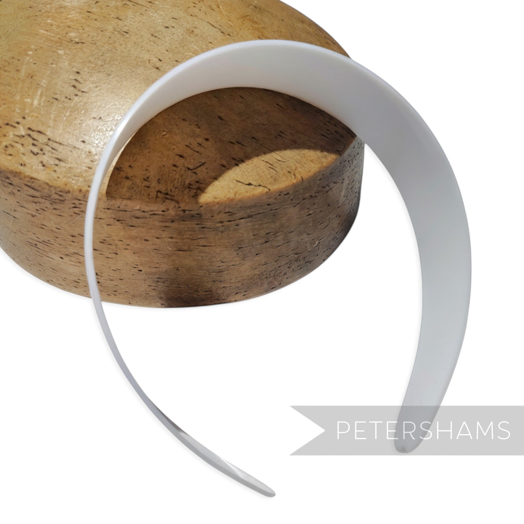 Petershams Millinery Supplies white plastic headband core blank for DIY hair accessory crafting on a wooden block